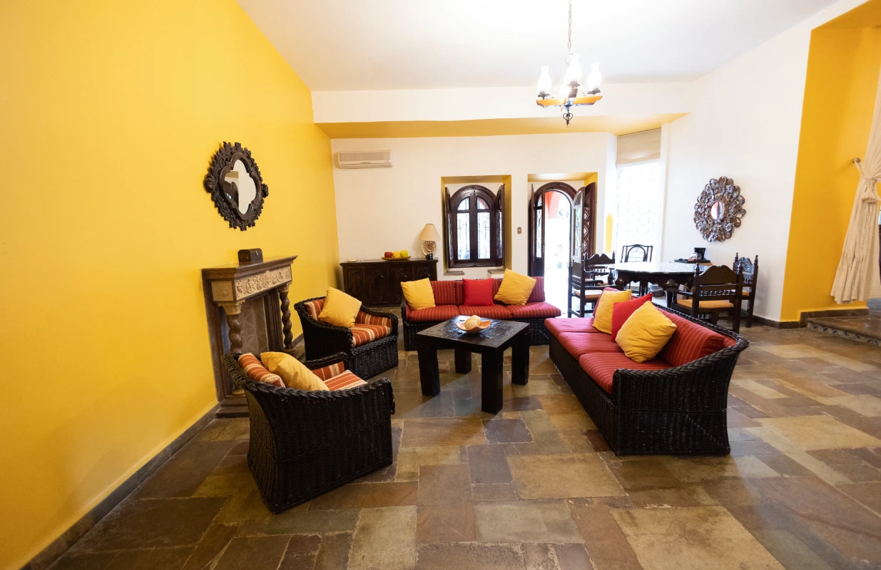 Sala con muebles de mimbre, paredes amarillas y mesa de comedor al fondo.