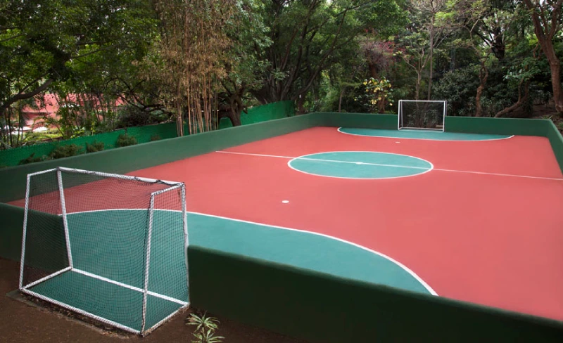 Cancha de f&uacute;tbol peque&ntilde;o, cercada, rodeada de &aacute;rboles y vegetaci&oacute;n.