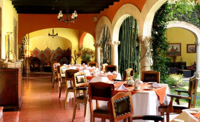 Restaurante con arquitectura colonial y mesas con manteles naranjas.