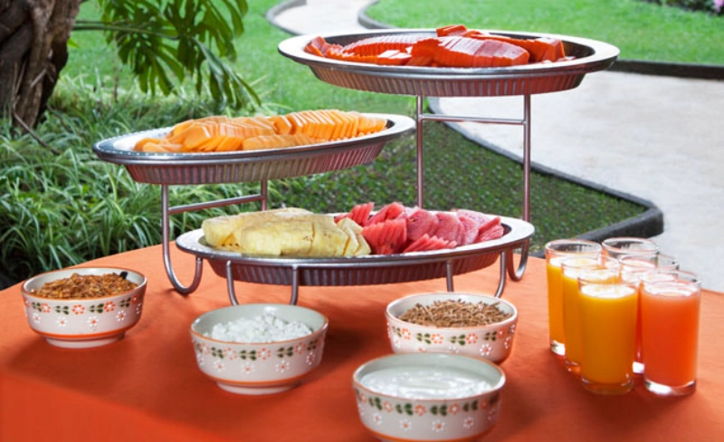 Frutas en bandejas, jugos y tazones sobre una mesa al aire libre.