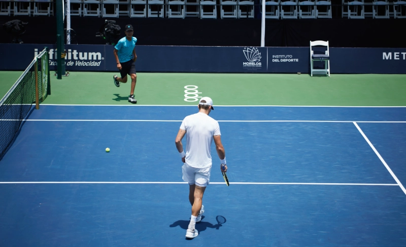 Jugador de tenis con vestimenta blanca en una cancha azul durante un partido.