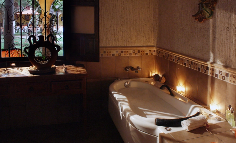 Ba&ntilde;o con ba&ntilde;era iluminada, velas y ventana al exterior.