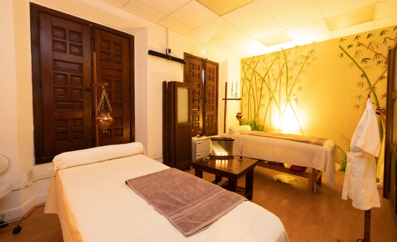 Sala de masajes con dos camas y luz tenue, decorada con bamb&uacute; en la pared.