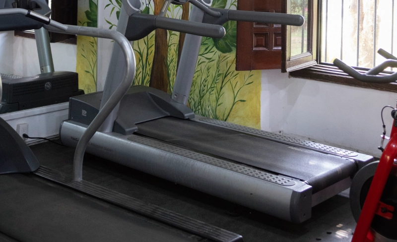 Cinta de correr en un gimnasio junto a una ventana y mural decorativo.