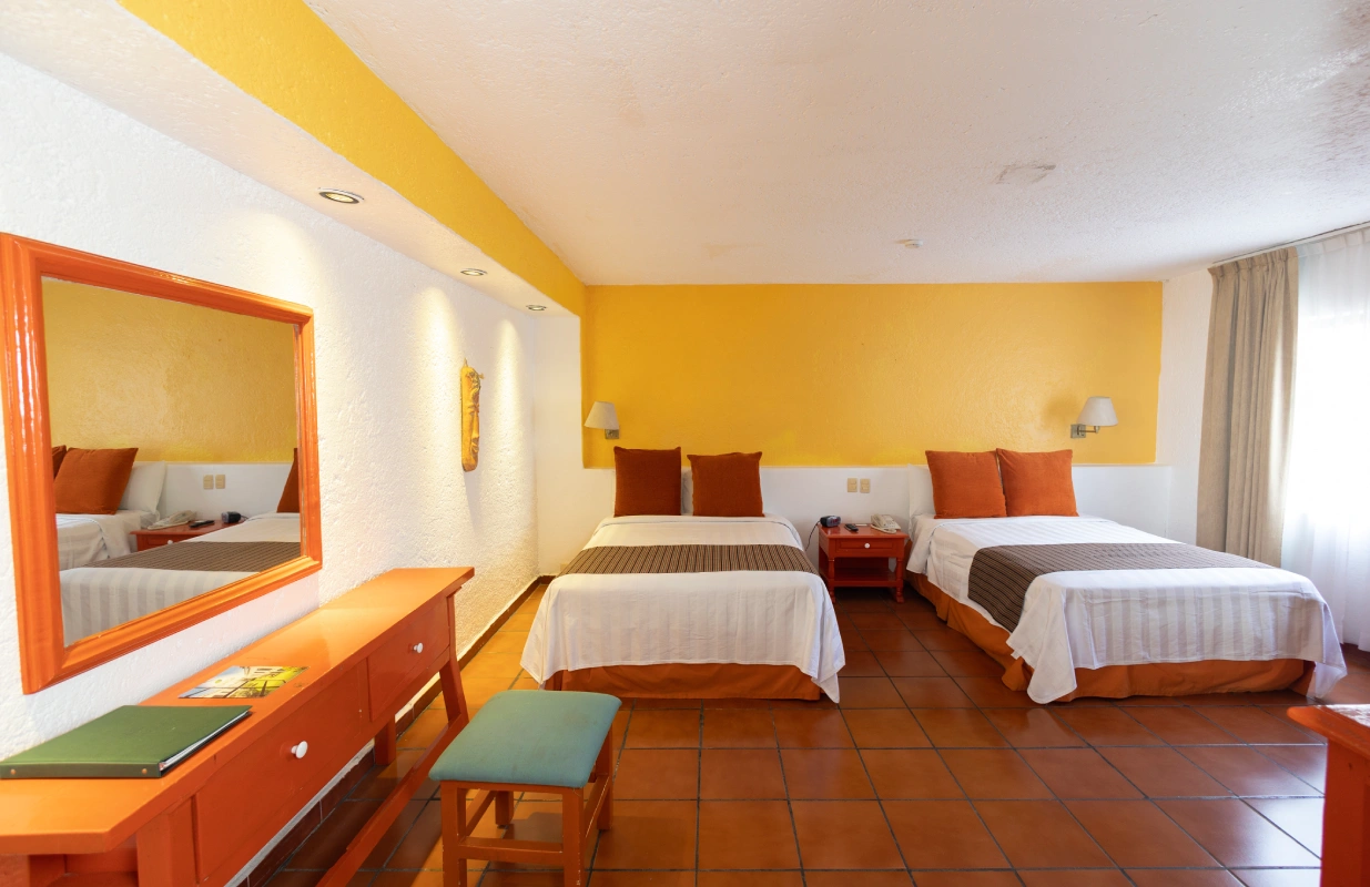 Habitaci&oacute;n de hotel con dos camas individuales, paredes amarillas y muebles naranjas.