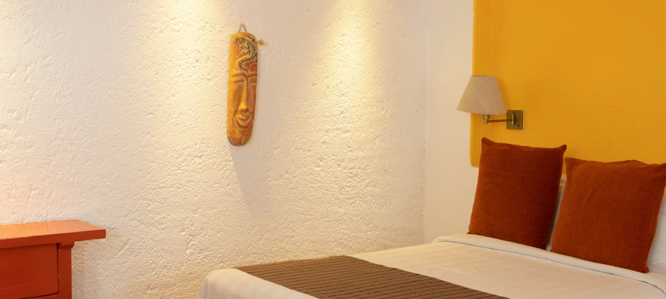 Habitaci&oacute;n con cama, cojines naranjas y adorno en pared blanca.