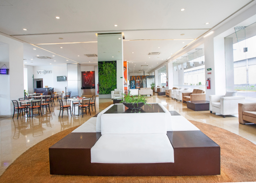 Lobby moderno con muebles blancos y marrones, y &aacute;rea de comedor al fondo.