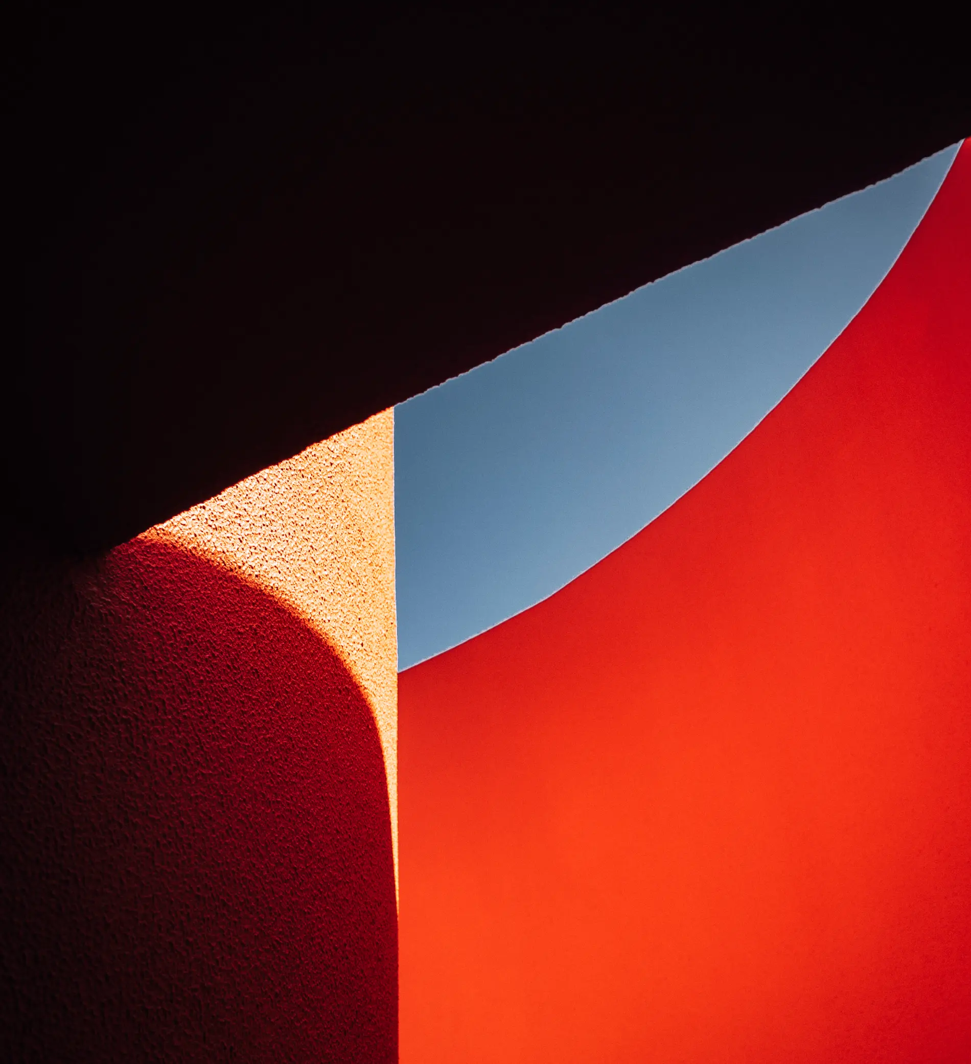 Abstrato de paredes curvas com sombras em tons de laranja e vermelho sob o c&eacute;u azul.