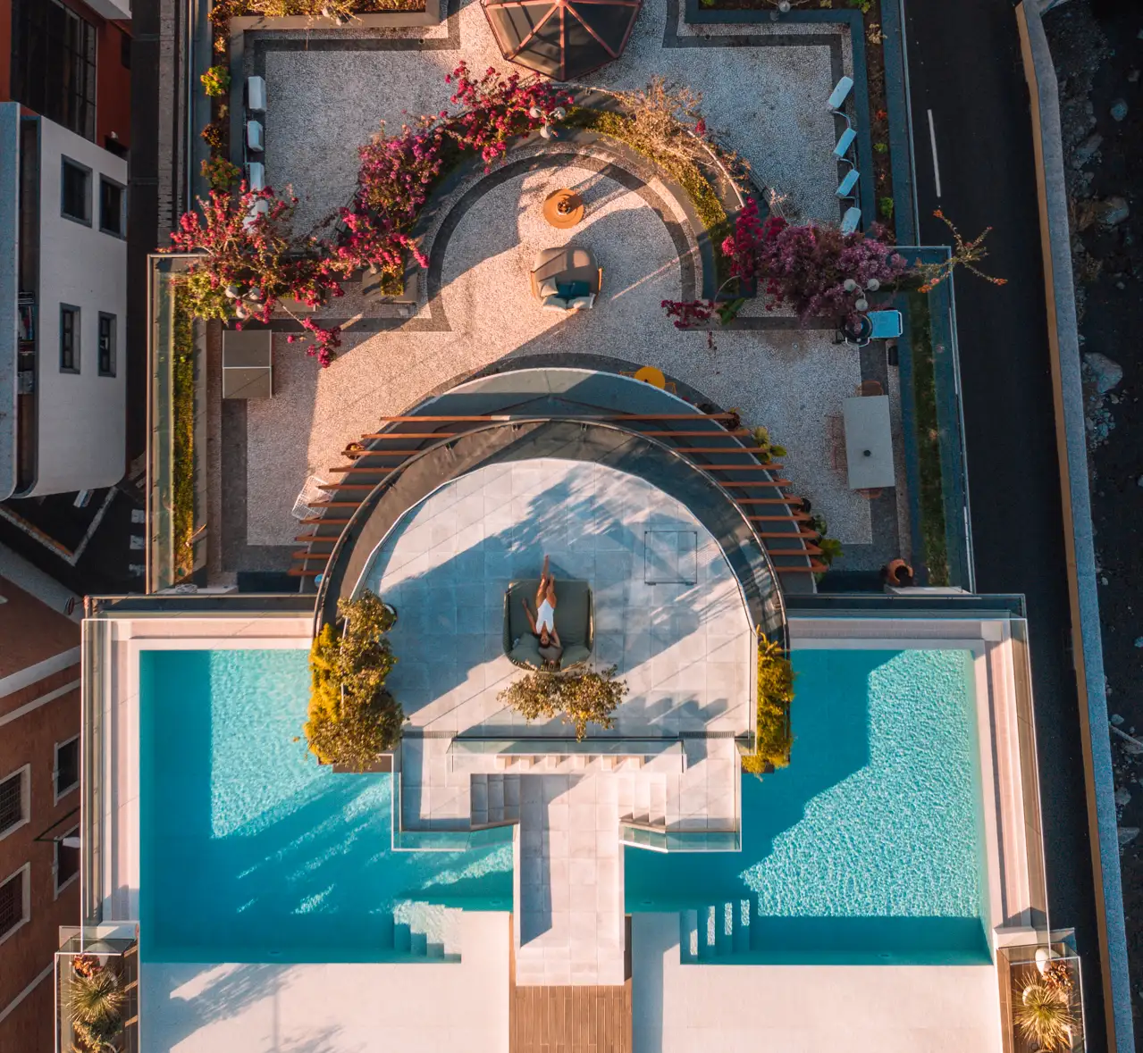 Vista a&eacute;rea de uma piscina e terra&ccedil;o com jardins e espregui&ccedil;adeiras.