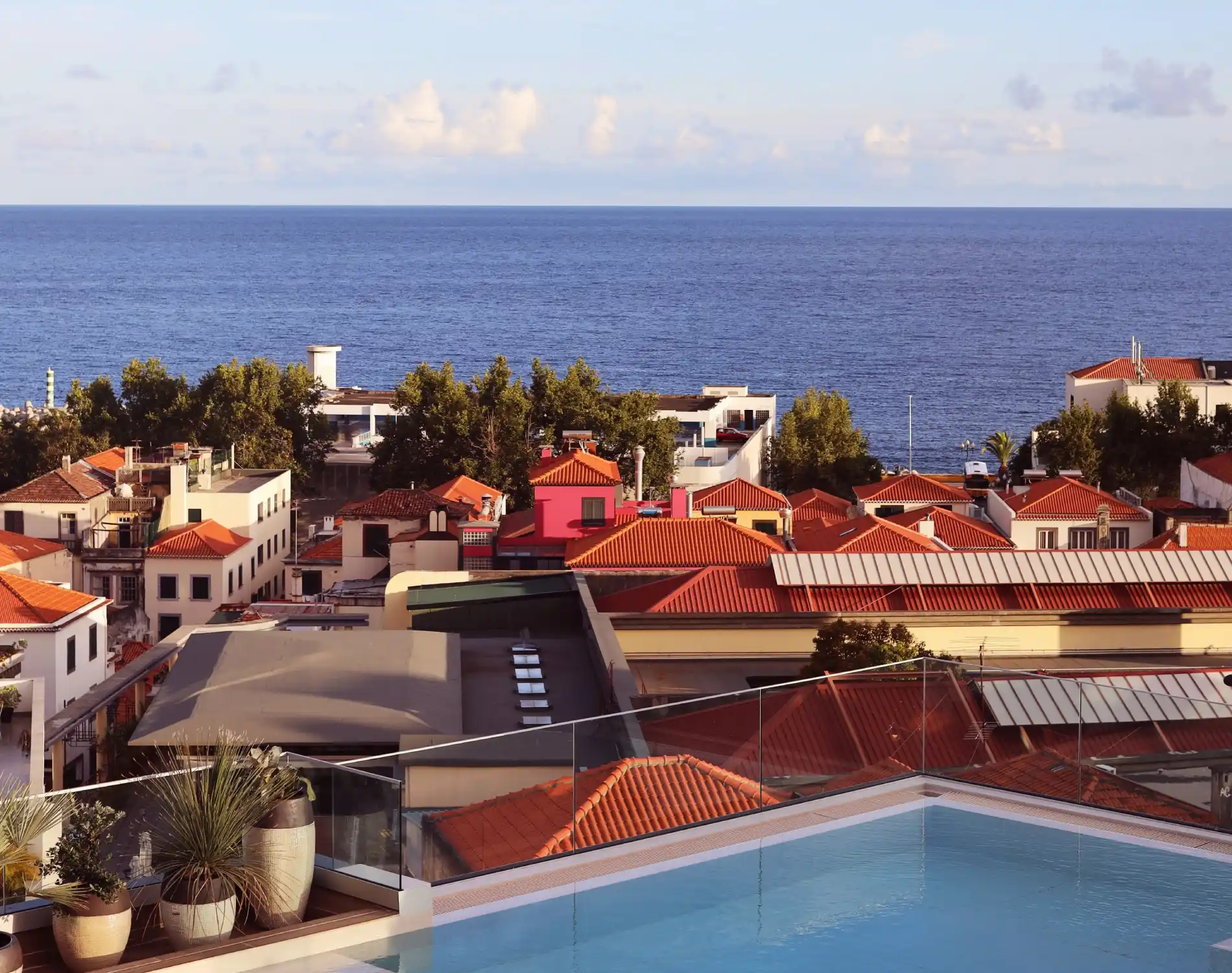 Vista de uma piscina em terra&ccedil;o com telhados vermelhos e o mar ao fundo.
