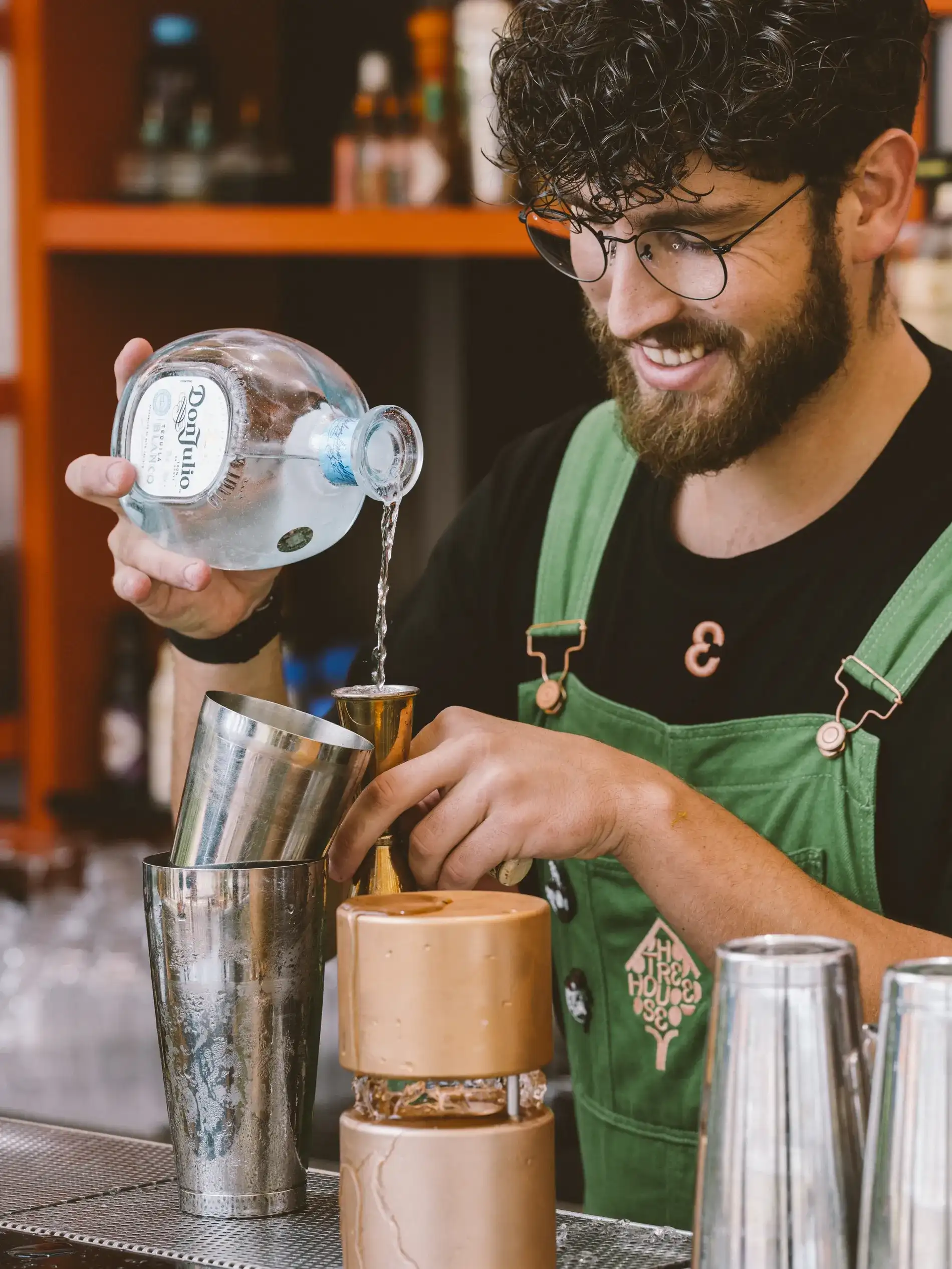 Homem prepara drink com bebida em bar, usando coqueteleira de metal.