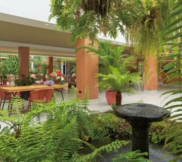 Jard&iacute;n interior con helechos, fuente y mesas rodeadas de follaje exuberante.