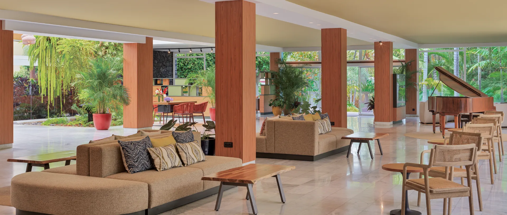 Sala moderna con sof&aacute;s, plantas y piano junto a ventanales.