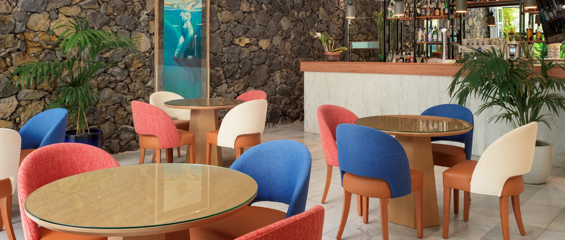Cafeter&iacute;a con mesas de madera y sillas de colores frente a una barra.