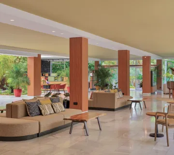 Lobby moderno con sof&aacute;s y mesas, rodeado de plantas.