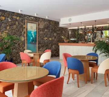Restaurante con sillas coloridas y pared de piedra detr&aacute;s de la barra.