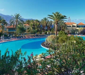 Piscina rodeada de palmeras y vegetaci&oacute;n exuberante en un d&iacute;a soleado.
