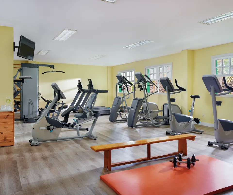 Gimnasio con bicicletas est&aacute;ticas, cintas de correr y pesas en un sal&oacute;n amplio.