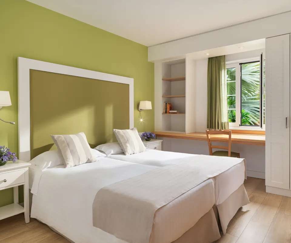 Habitaci&oacute;n moderna con camas gemelas, escritorio y ventana con cortina verde.
