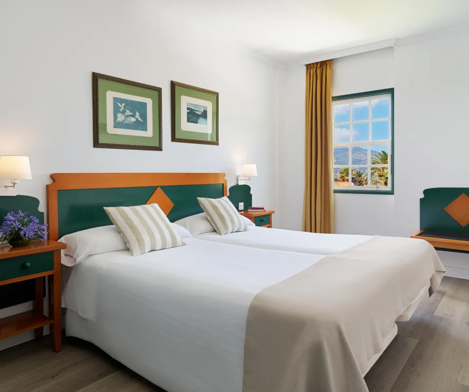 Habitaci&oacute;n de hotel con camas individuales y ventana con vista al exterior.