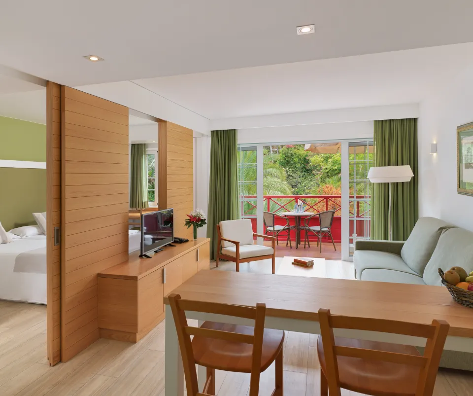 Sala moderna con sof&aacute;, TV, mesa de comedor y balc&oacute;n con vista a jardines.