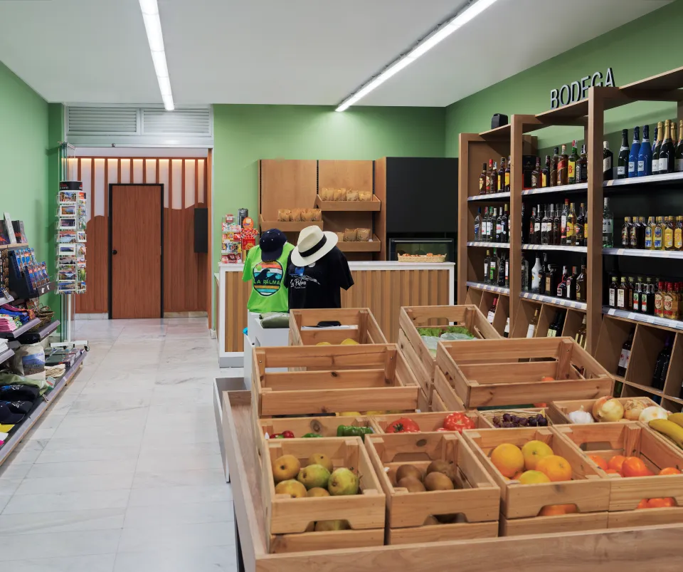 Tienda con frutas, licores y ropa en exhibici&oacute;n con paredes verdes.