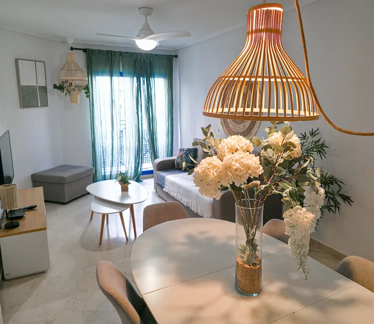 Sala luminosa con mesa, flores y sofá; lámpara de diseño moderno colgante.