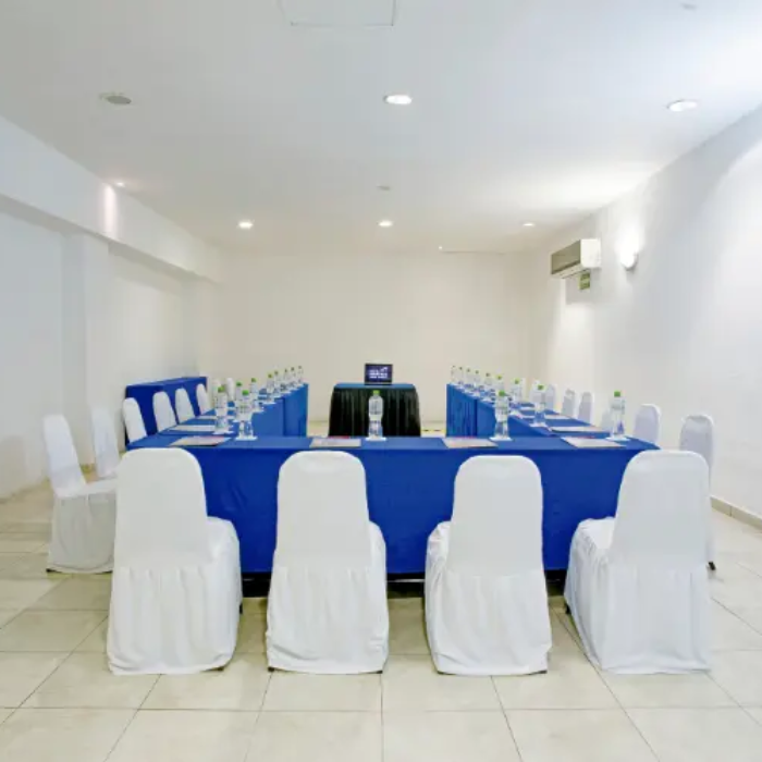 Sala de conferencia en forma de U con sillas blancas y mantel azul.