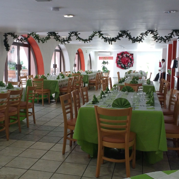 Sal&oacute;n decorado para evento con mesas y sillas, manteles verdes y guirnaldas.