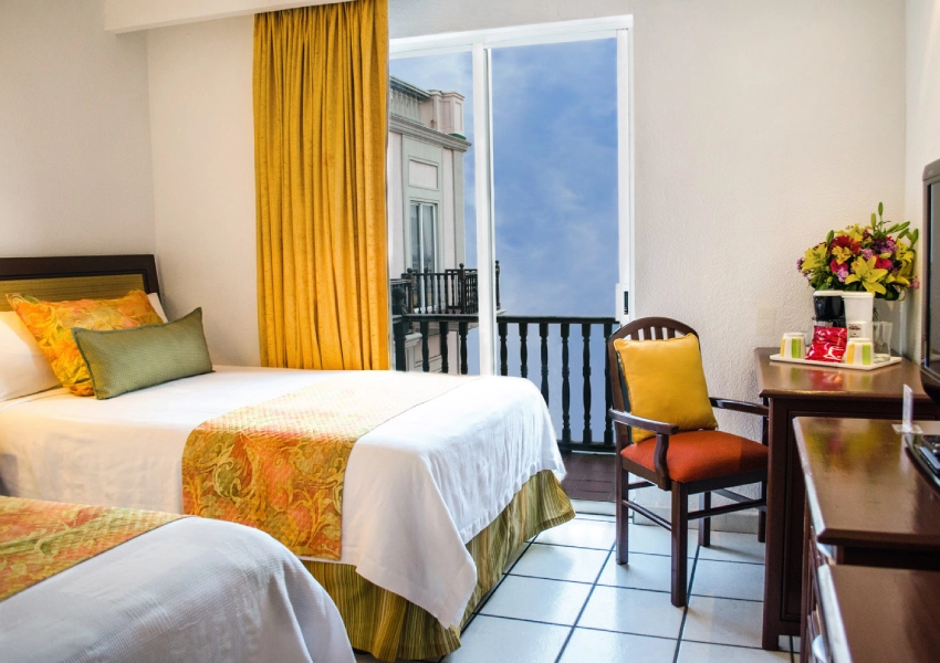 Habitaci&oacute;n con camas, flores y ventana con vista.