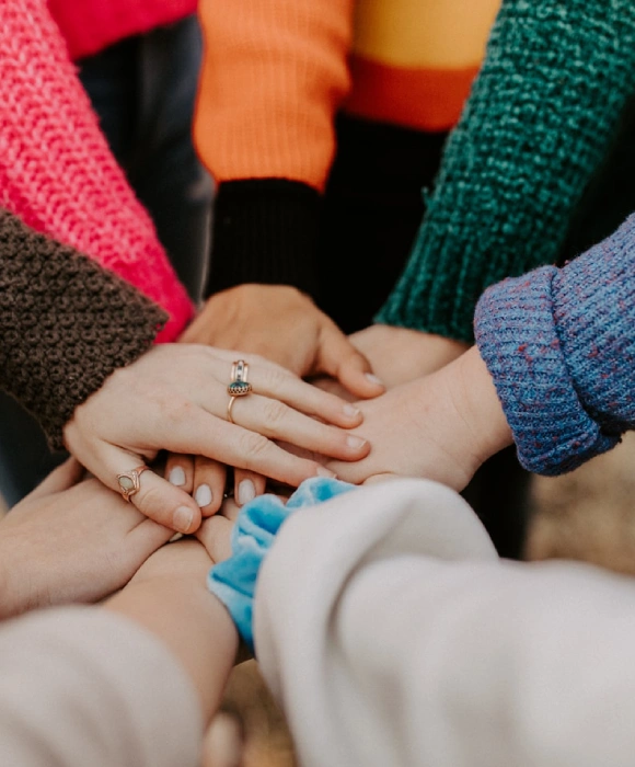 Manos de varias personas unidas en equipo, con su&eacute;teres coloridos.