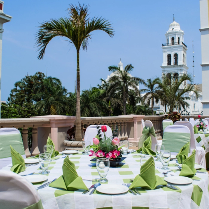 Mesa elegante con flores, manteles verdes y una iglesia al fondo.