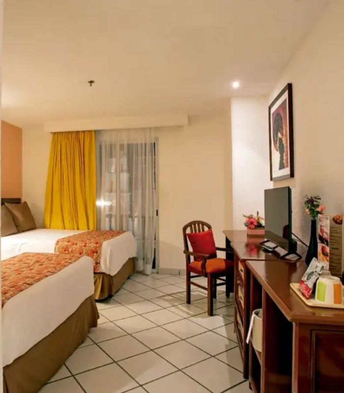 Habitaci&oacute;n de hotel con dos camas y escritorio, iluminada y decorada.