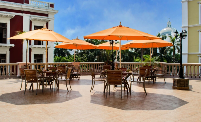 Terraza con sombrillas naranjas y muebles de madera, rodeada de edificios cl&aacute;sicos.