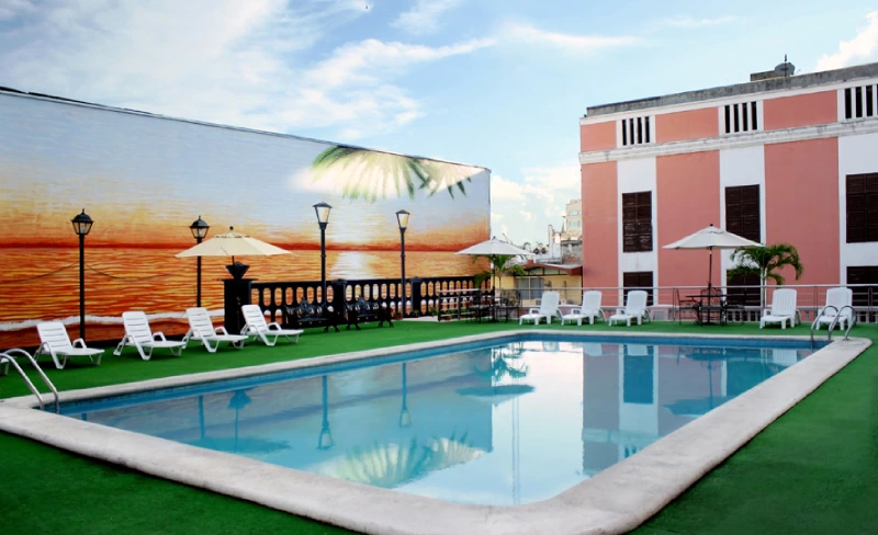 Piscina en azotea con sillas blancas, mural de atardecer y cielo azul.
