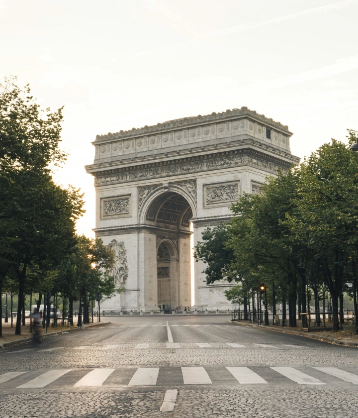 Arc de Triomphe entour&eacute; d'arbres et rue d&eacute;serte le matin.