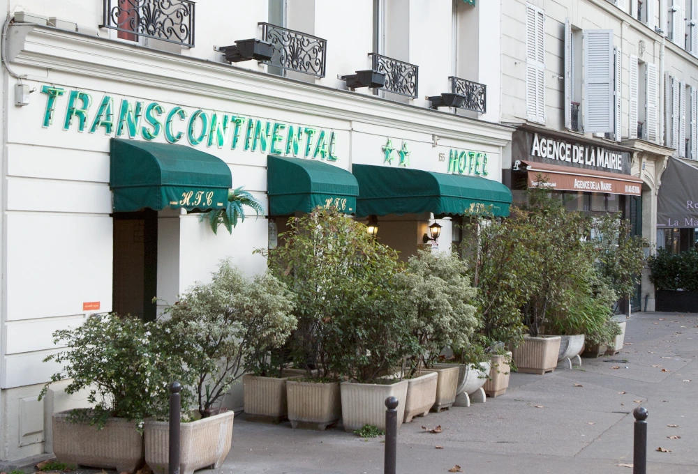 Fa&ccedil;ade d'un h&ocirc;tel "Transcontinental" avec auvent vert et plantes.