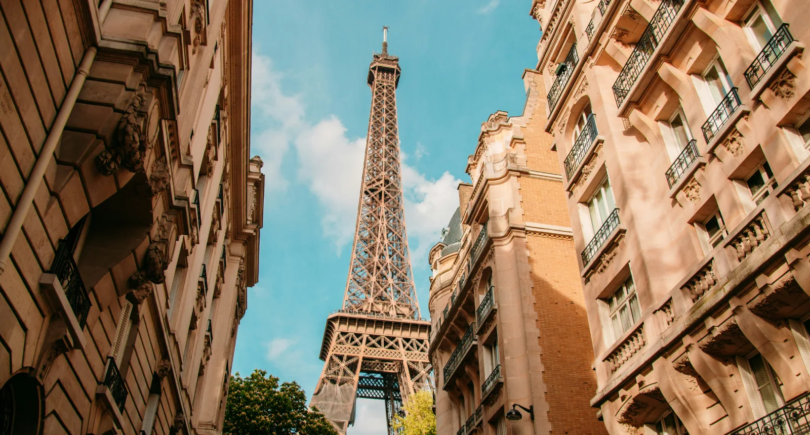 Vue de la tour Eiffel entre deux immeubles parisiens sous un ciel bleu.
