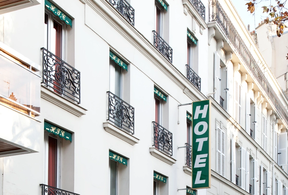 Fa&ccedil;ade d'h&ocirc;tel parisien avec balcons en fer forg&eacute; et enseigne verte.