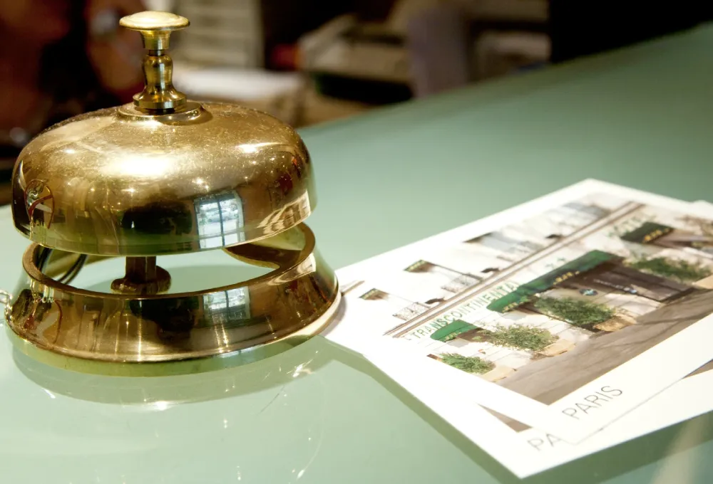 Sonnette de r&eacute;ception en laiton pr&egrave;s de brochures d'h&ocirc;tel sur un comptoir en verre.