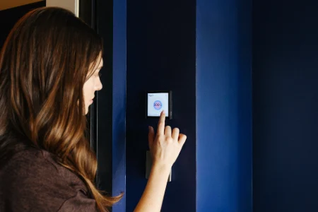 Mujer ajustando un termostato en una pared azul.