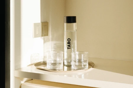 Botella de agua y tres vasos sobre una bandeja en una encimera blanca.