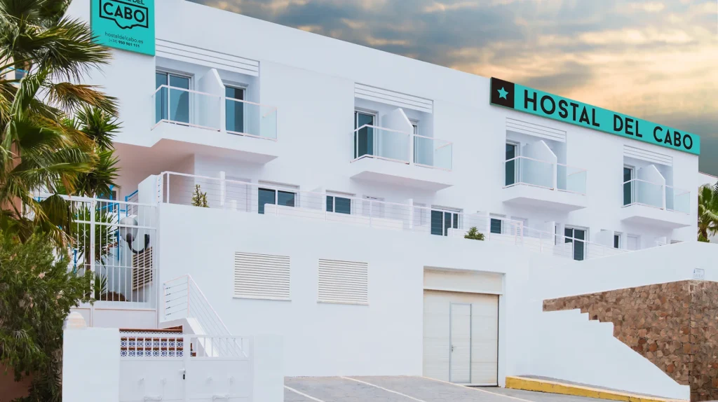 Edificio blanco del Hostal del Cabo con cielo nuboso al fondo.