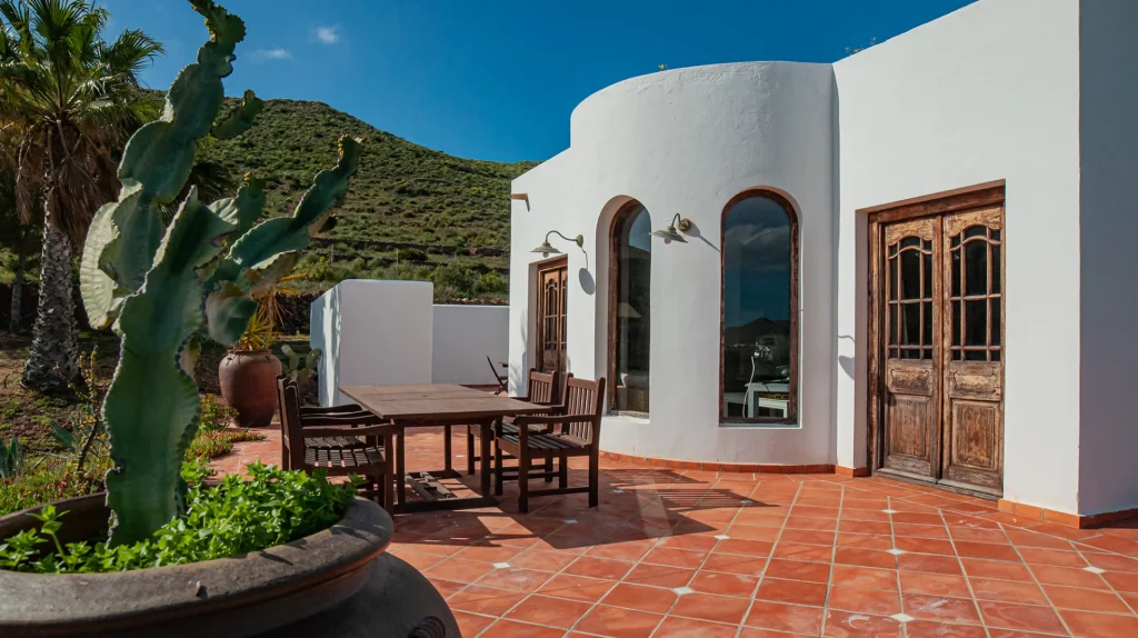 Casa blanca con terraza de terracota y monta&ntilde;a verde al fondo.