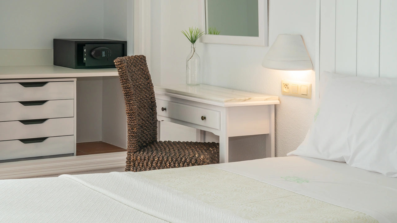 Habitaci&oacute;n de hotel con escritorio, silla de mimbre y caja fuerte.