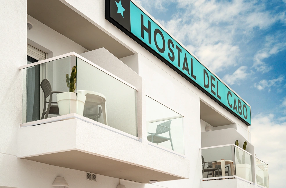 Balc&oacute;n del Hostal del Cabo con sillas y planta, cielo despejado al fondo.