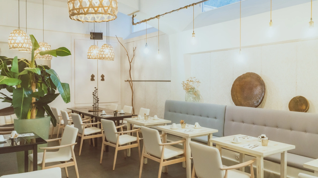 Comedor elegante con mesas blancas y sillas junto a plantas grandes.