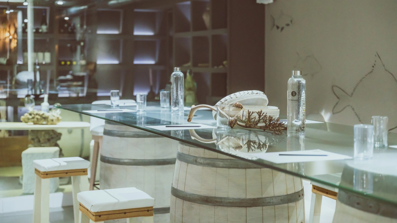 Mesa de vidrio sobre barriles, con botellas y decoraci&oacute;n marina.