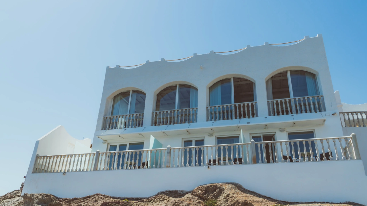 Casa blanca de dos pisos con balcones amplios bajo un cielo despejado.
