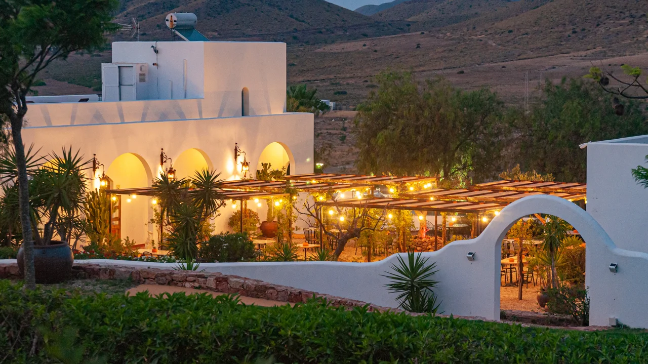 Terraza iluminada con luces c&aacute;lidas al atardecer, rodeada de monta&ntilde;as.